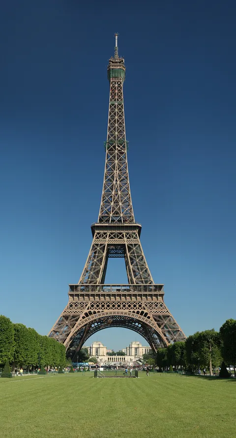 The Eiffel Tower in sunshine under a clear blue sky, seen from the lawns of the Champ de Mars
